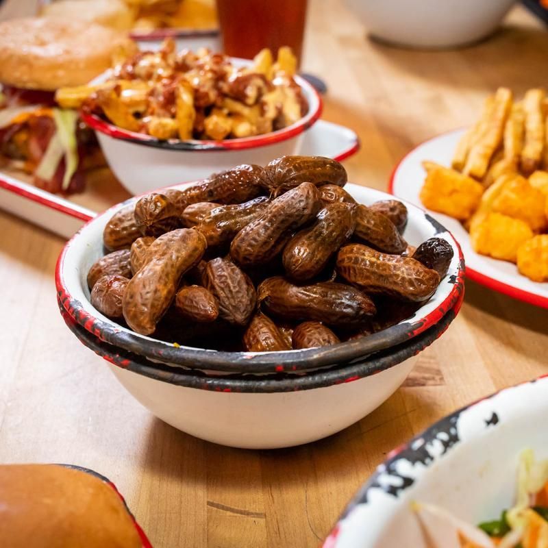 A bowl of peanuts sits on a table next to other bowls of food