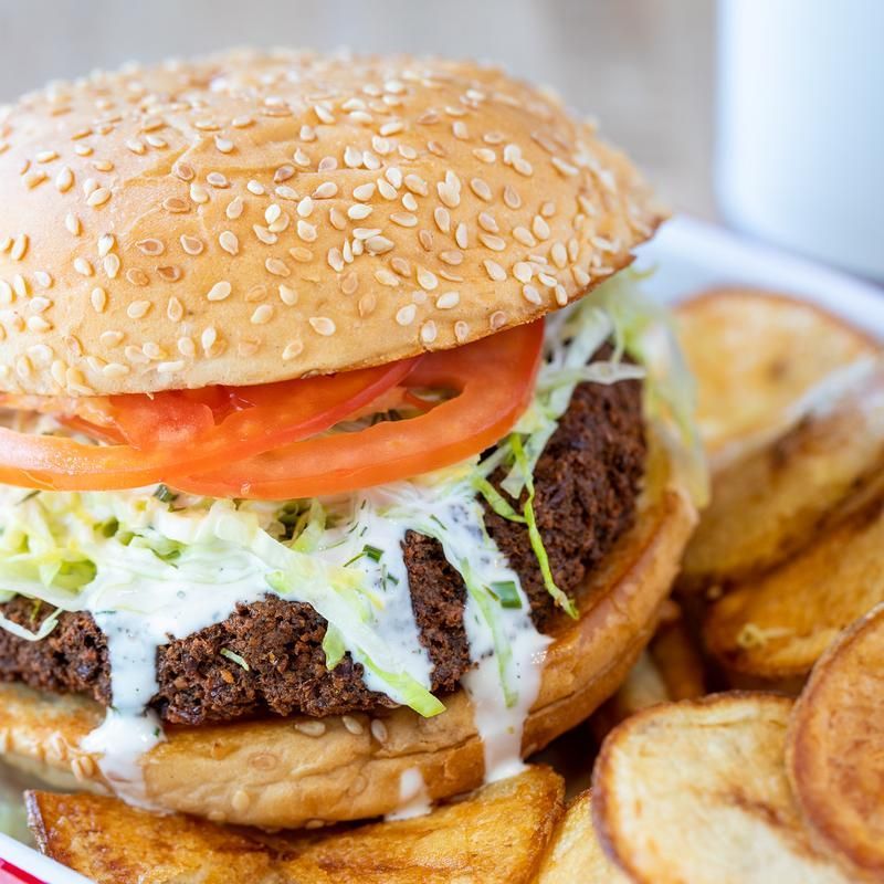 A close up of a hamburger with lettuce , tomato and french fries on a plate.