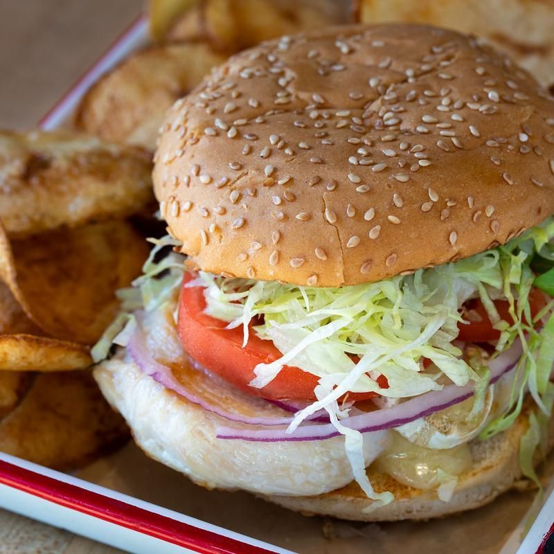 A hamburger with lettuce tomato and onions next to potato chips