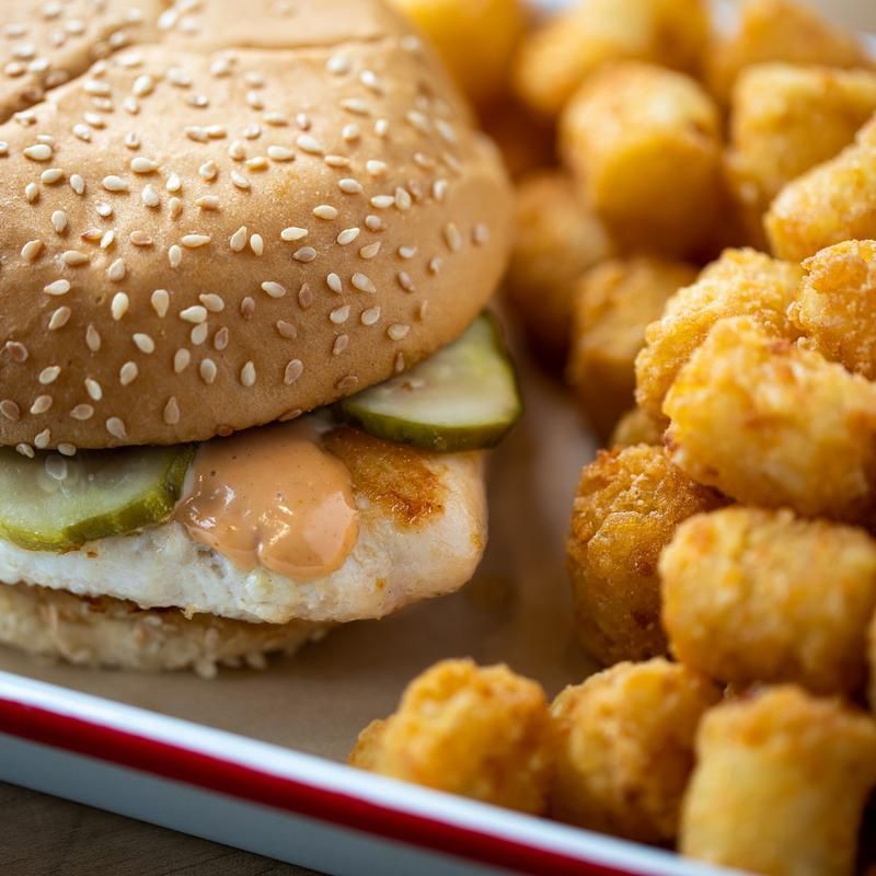 A close up of a chicken sandwich and tots in a box.