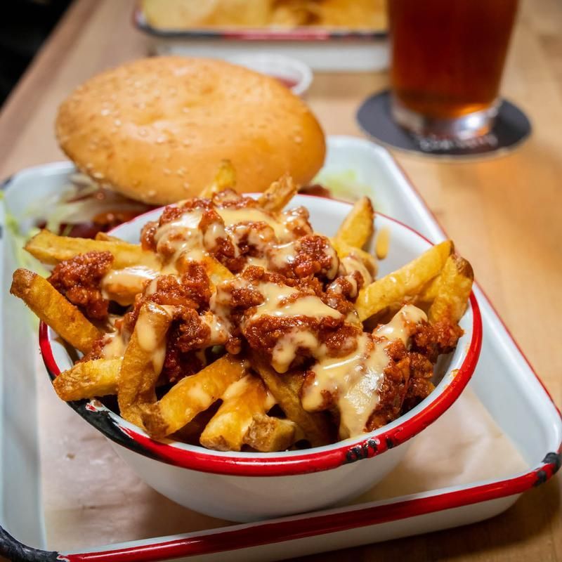 A bowl of chili cheese fries on a tray next to a hamburger