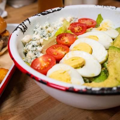 A bowl of food with eggs , tomatoes , lettuce and avocado on a table.