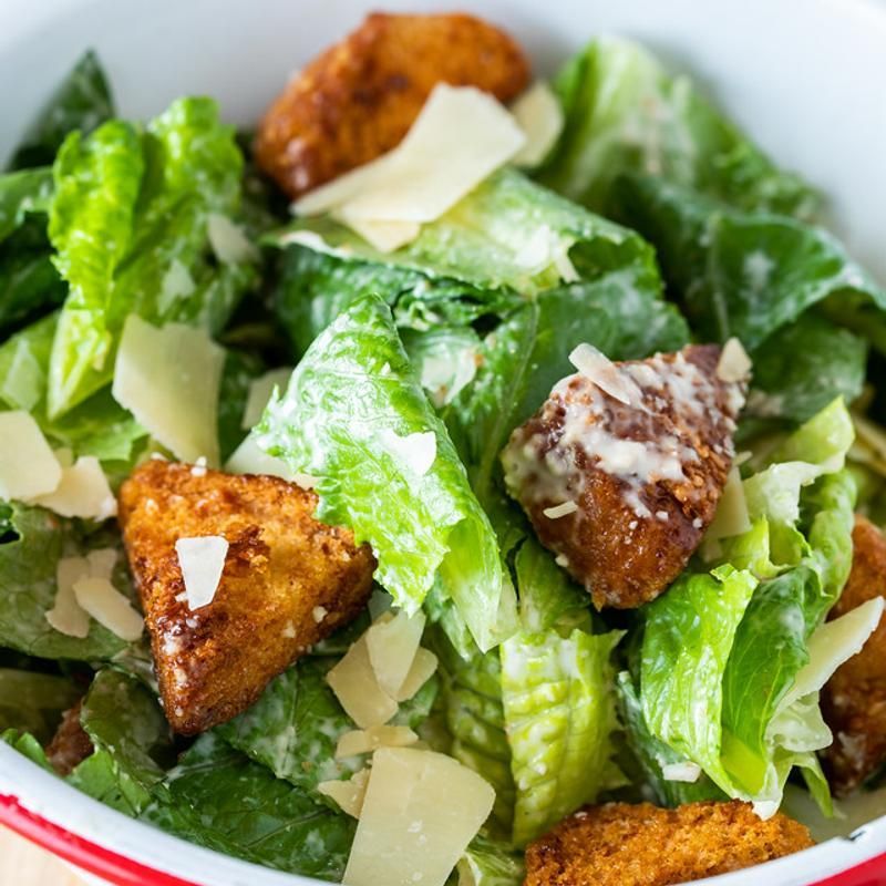 A close up of a salad with lettuce , croutons and cheese in a bowl.