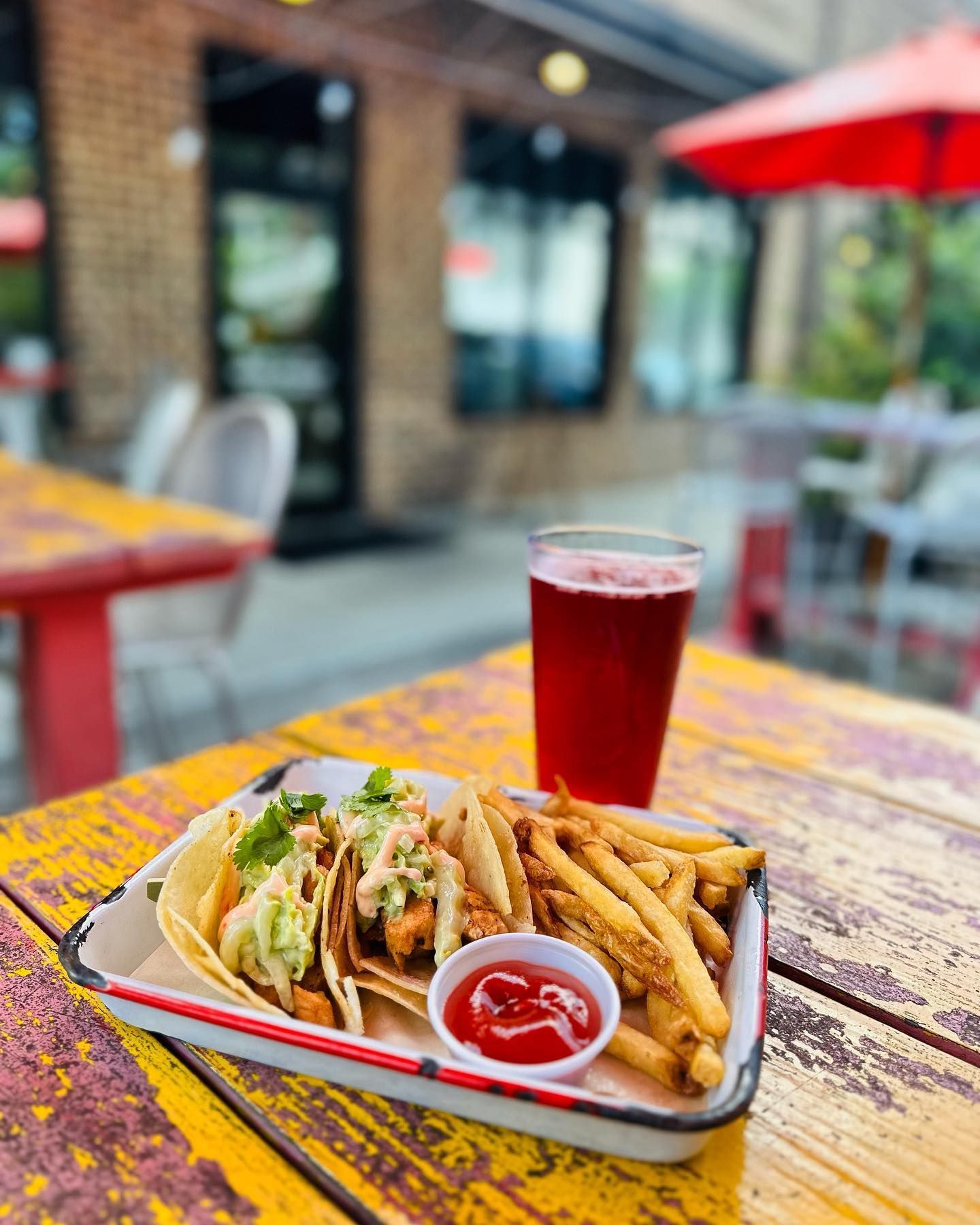 A tray of tacos and french fries on a table with a glass of beer.