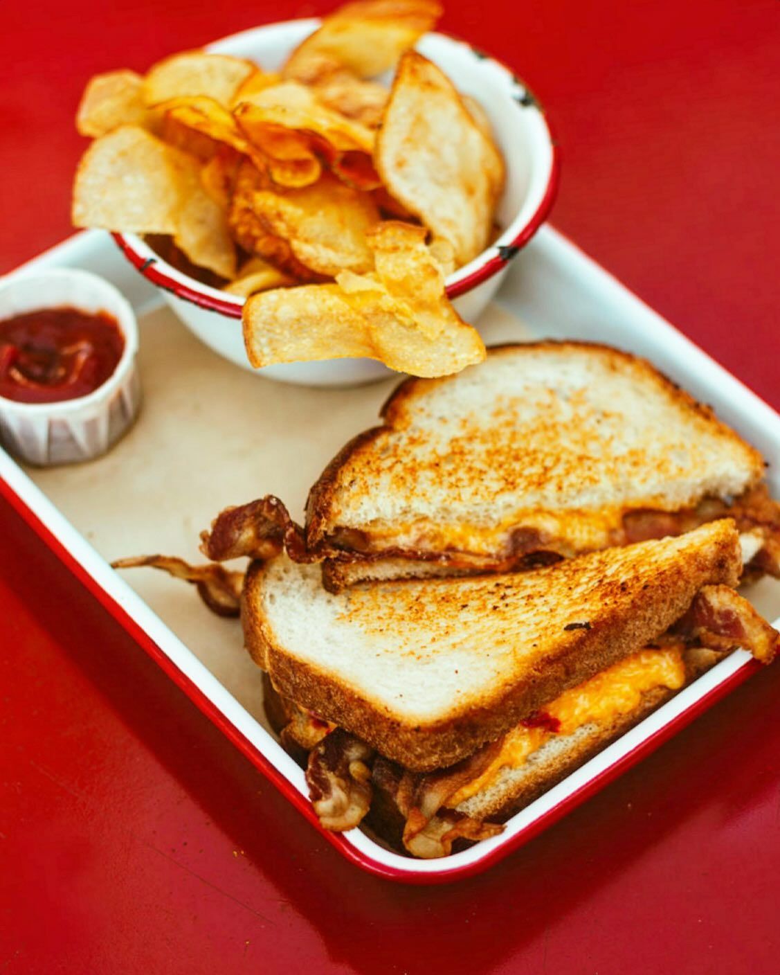 A grilled cheese sandwich and a bowl of potato chips on a tray
