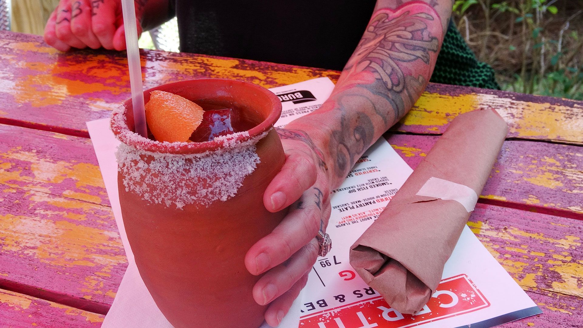 a person with a tattoo on their arm is holding a cup of drink with a straw