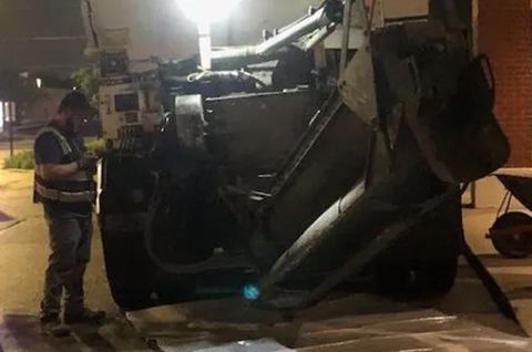 A worker in a safety vest inspects an overturned concrete mixer on a city street at night.