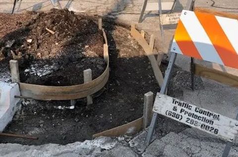 Construction site: Curved wooden form for concrete curb, dirt pile, orange and white traffic barrier.