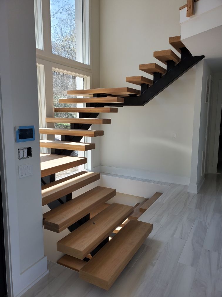 Modern floating wooden staircase with open treads in a bright, empty interior near tall windows
