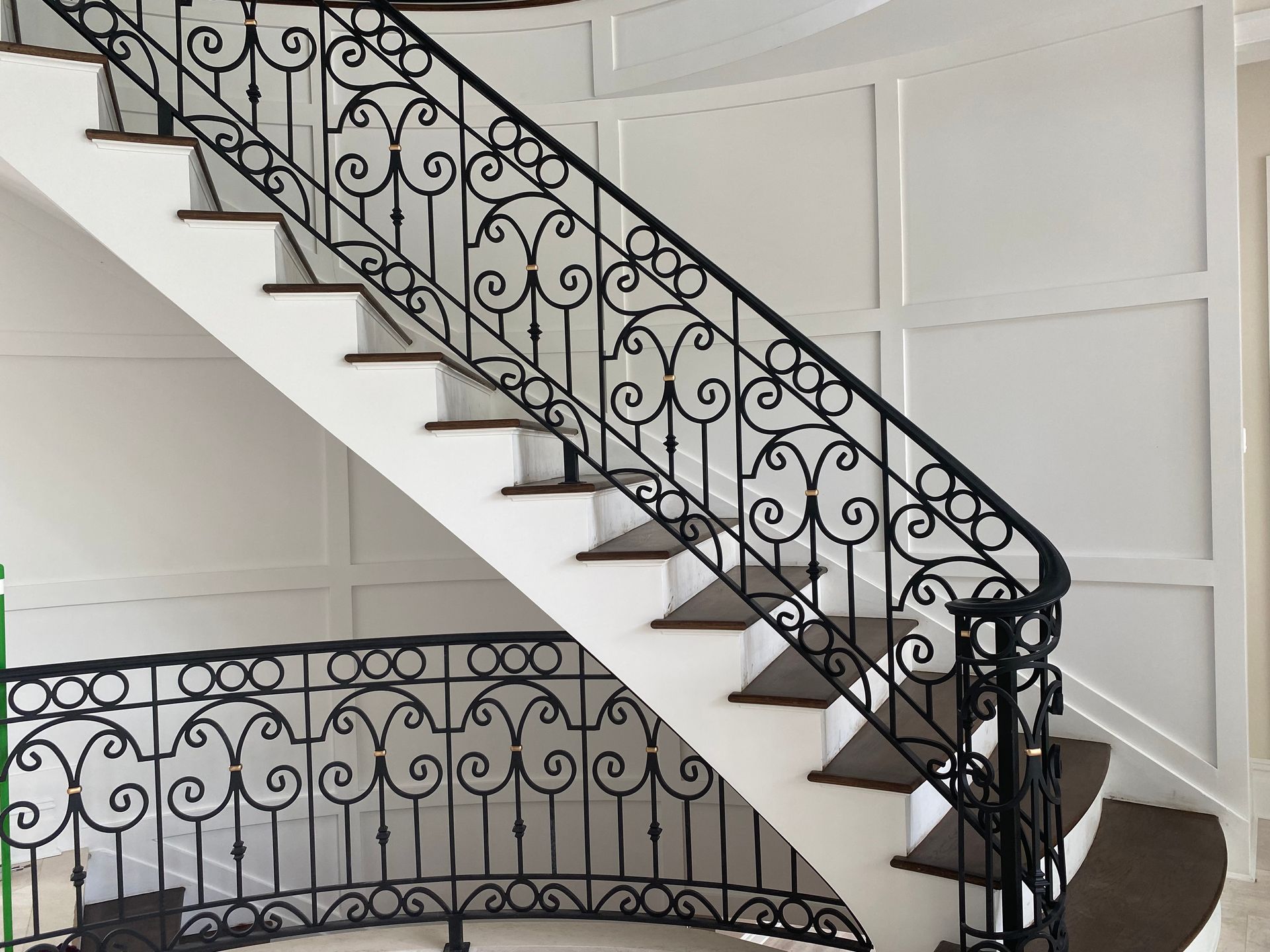 Black wrought-iron staircase railing with decorative scrollwork in a bright interior stairwell