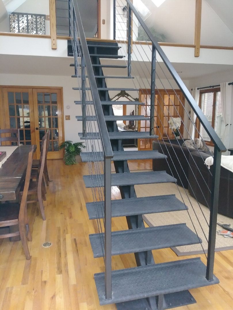 Indoor loft with black staircase, wood floors, and a metal railing in a bright room