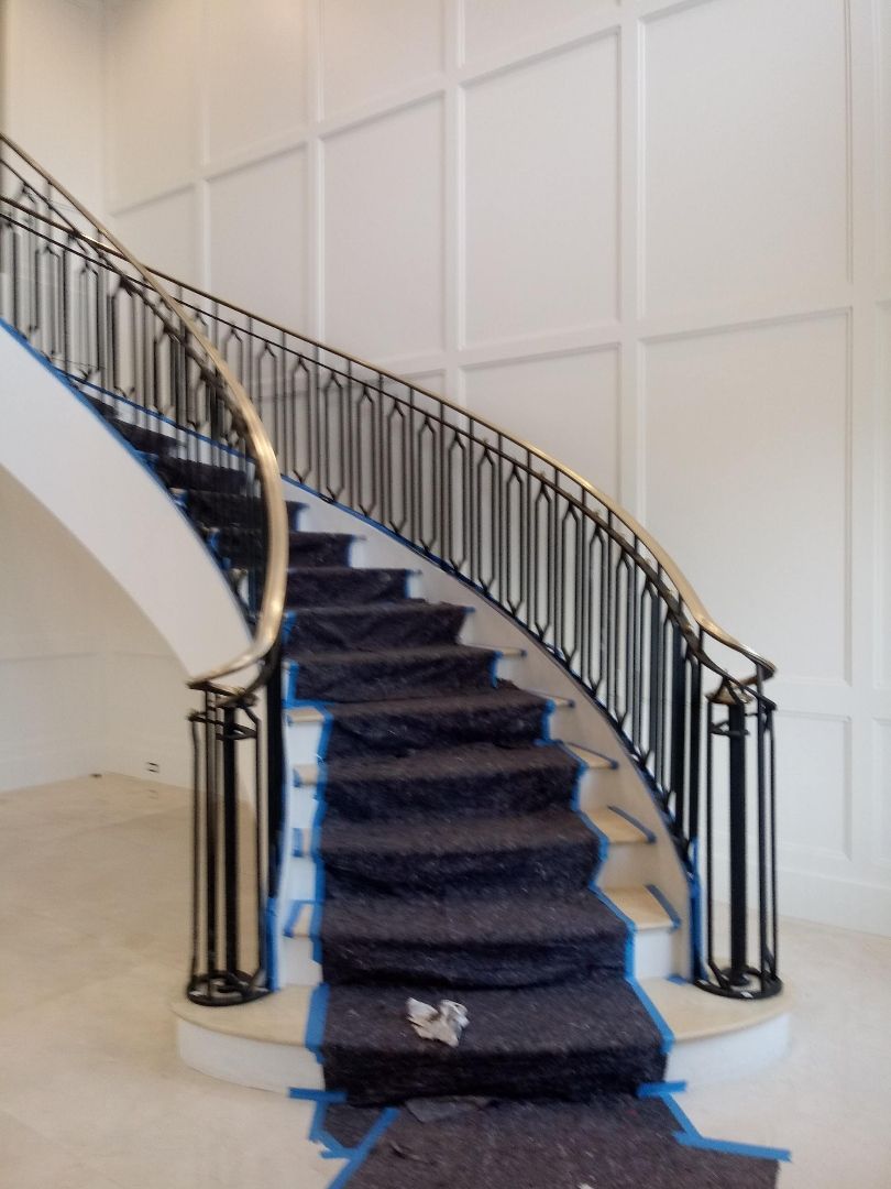 Curved staircase with dark carpet runner and ornate black railings against a white paneled wall