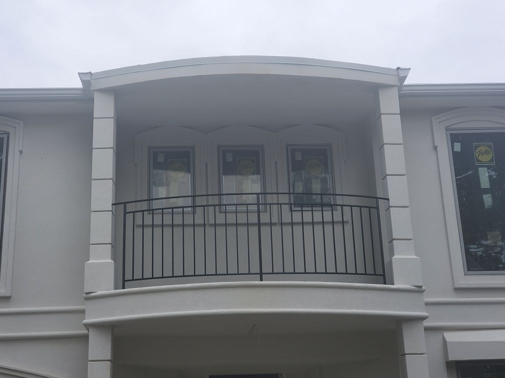 Second-floor balcony with black railing on a light gray building facade