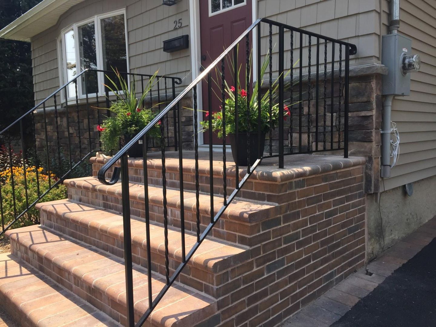 Brick front steps with black metal railing and flower planters leading to a house entrance
