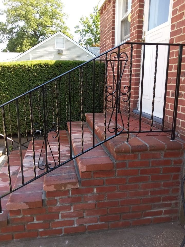 Brick front steps with black metal railing beside a red brick house and green hedge