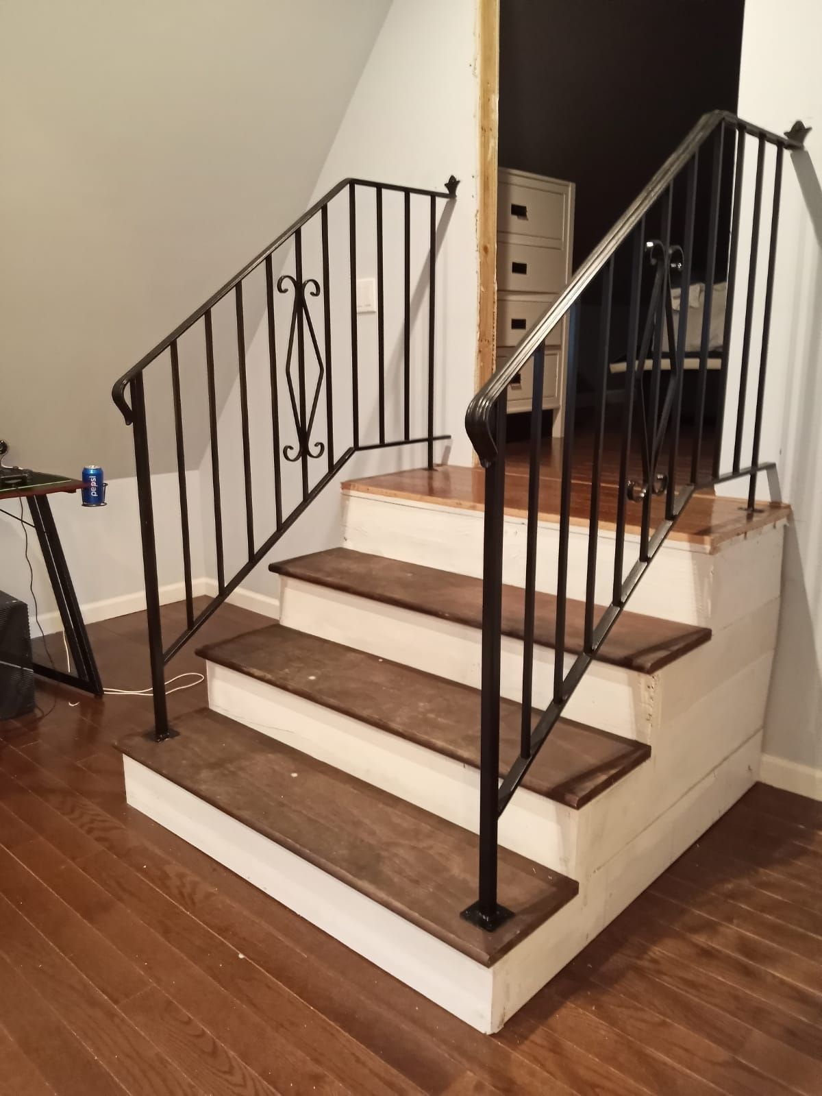 Indoor staircase with wooden steps, white risers, and black iron railings against a cream wall.