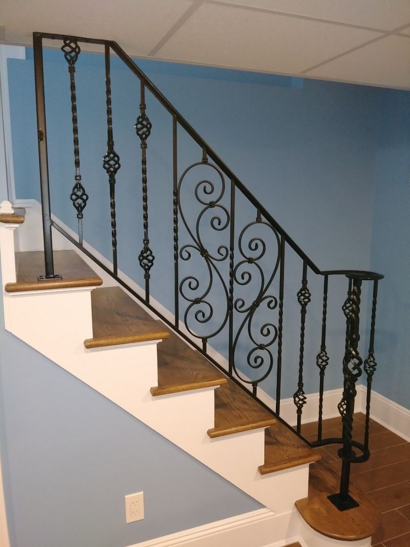 Indoor staircase with white steps, wooden treads, blue walls, and ornate black iron railing