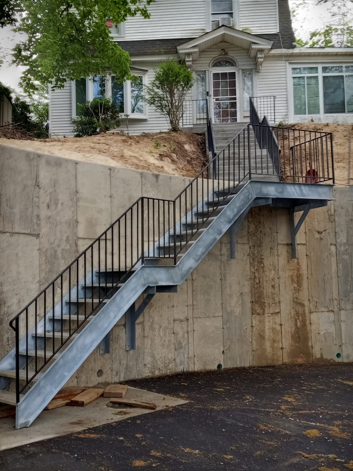 Exterior staircase with black railings leading up a retaining wall to a house entrance