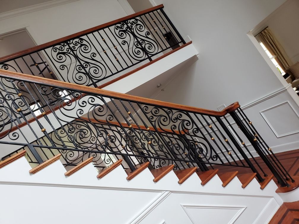 Interior staircase with ornate black iron railing and wooden steps in a bright home.