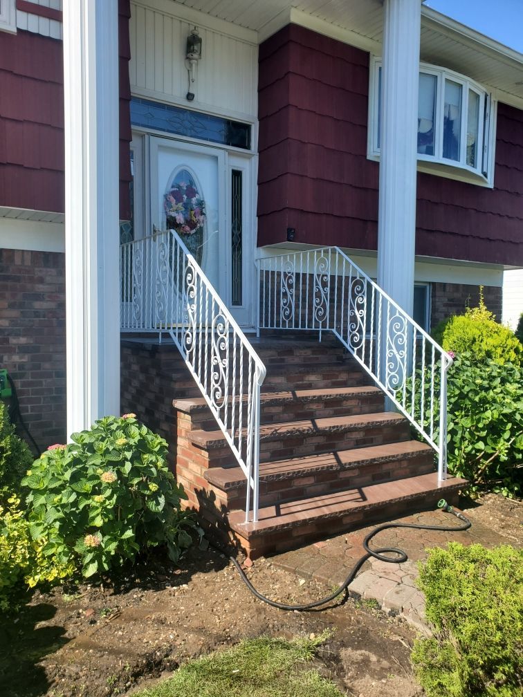 Front steps with white railing leading to a house entry with a blue door and brick facade.