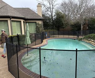 A worker installing a black mesh safety fence around a backyard swimming pool.