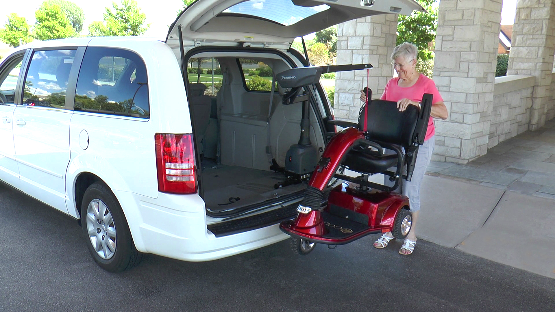 A woman is loading a mobility scooter into the back of a van.