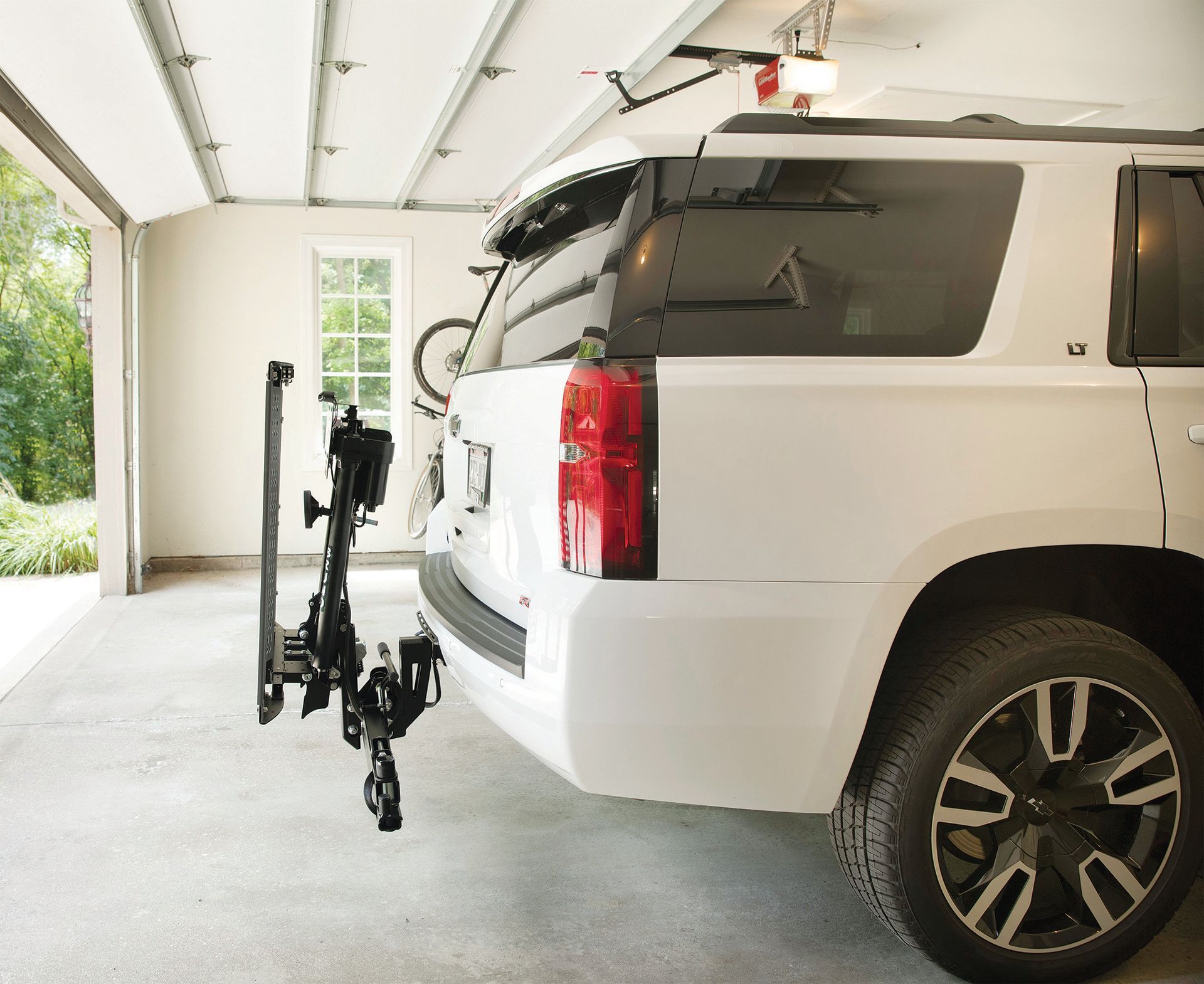 A white suv is parked in a garage with a bike rack attached to the back.