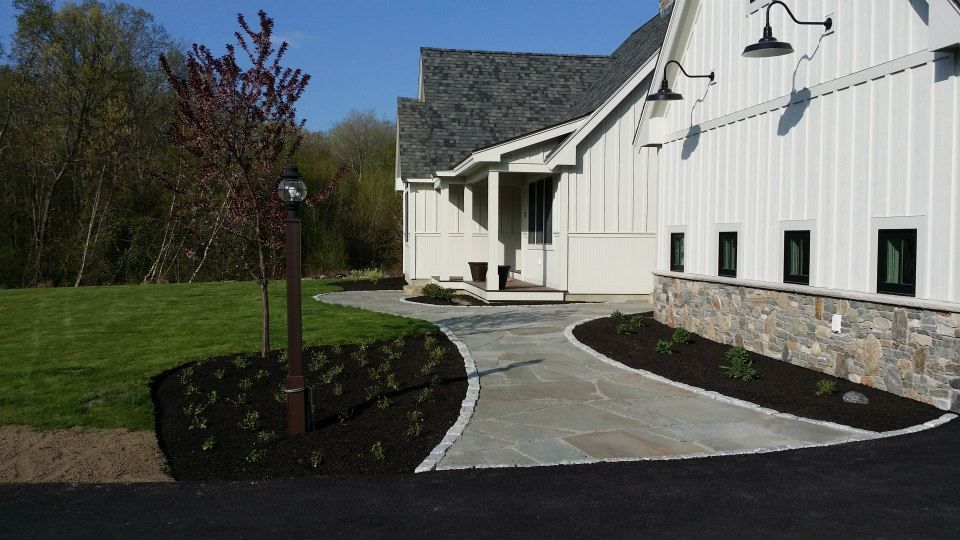 A white house with a stone wall and a driveway leading to it.