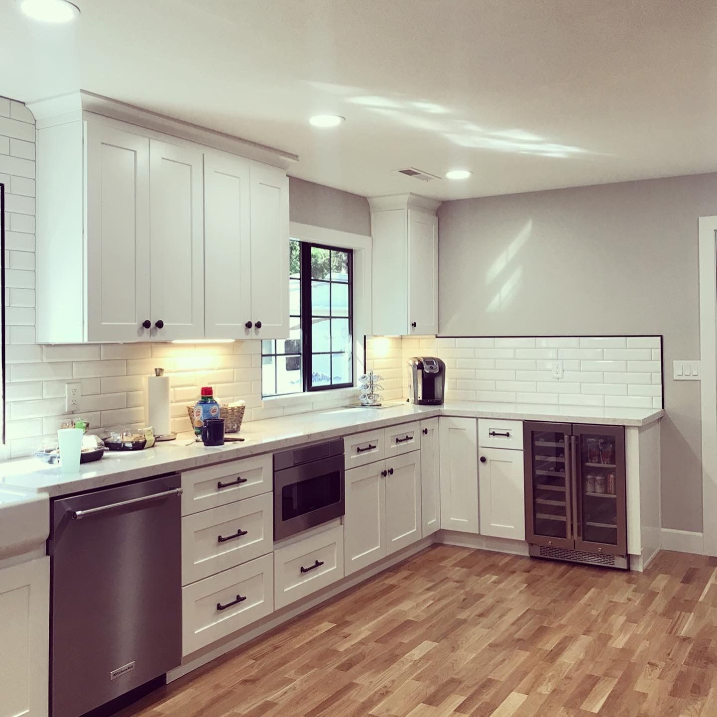 A kitchen with white cabinets , stainless steel appliances , a wine cooler and a window.