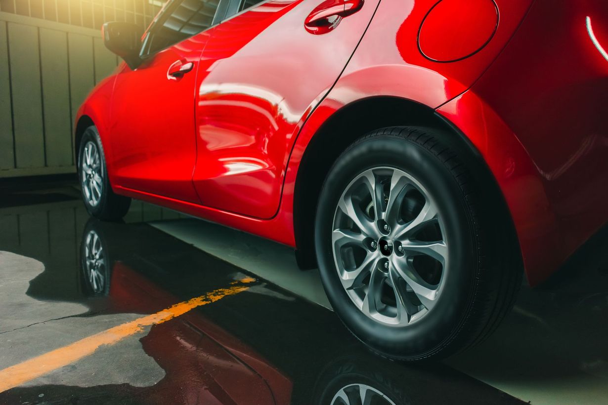Red car parked on wet, reflective surface next to yellow parking line.