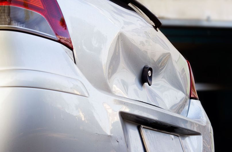 White car with a large dent in the rear, damage from a collision.