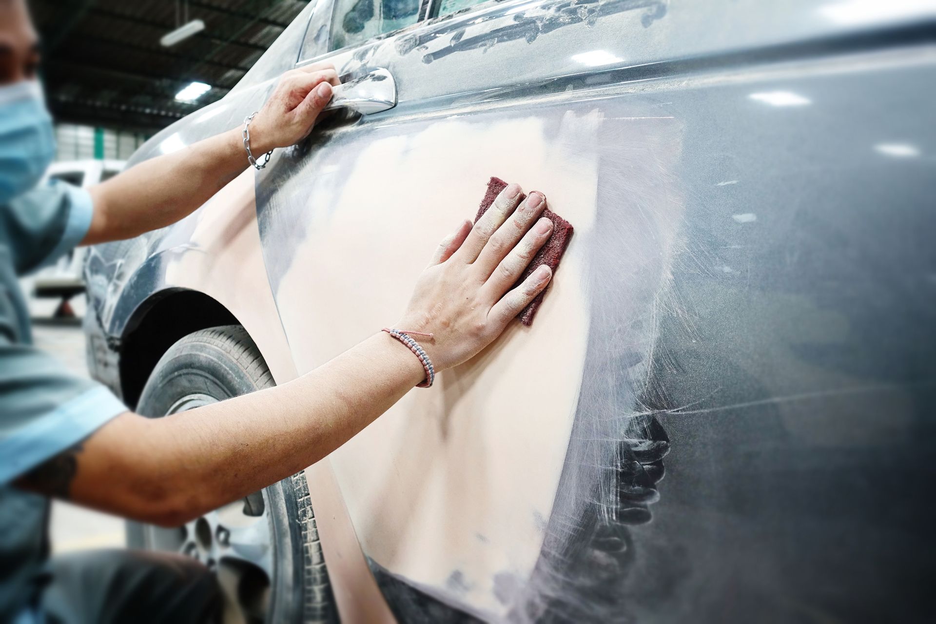 Person sanding a car door covered in filler, in a workshop.