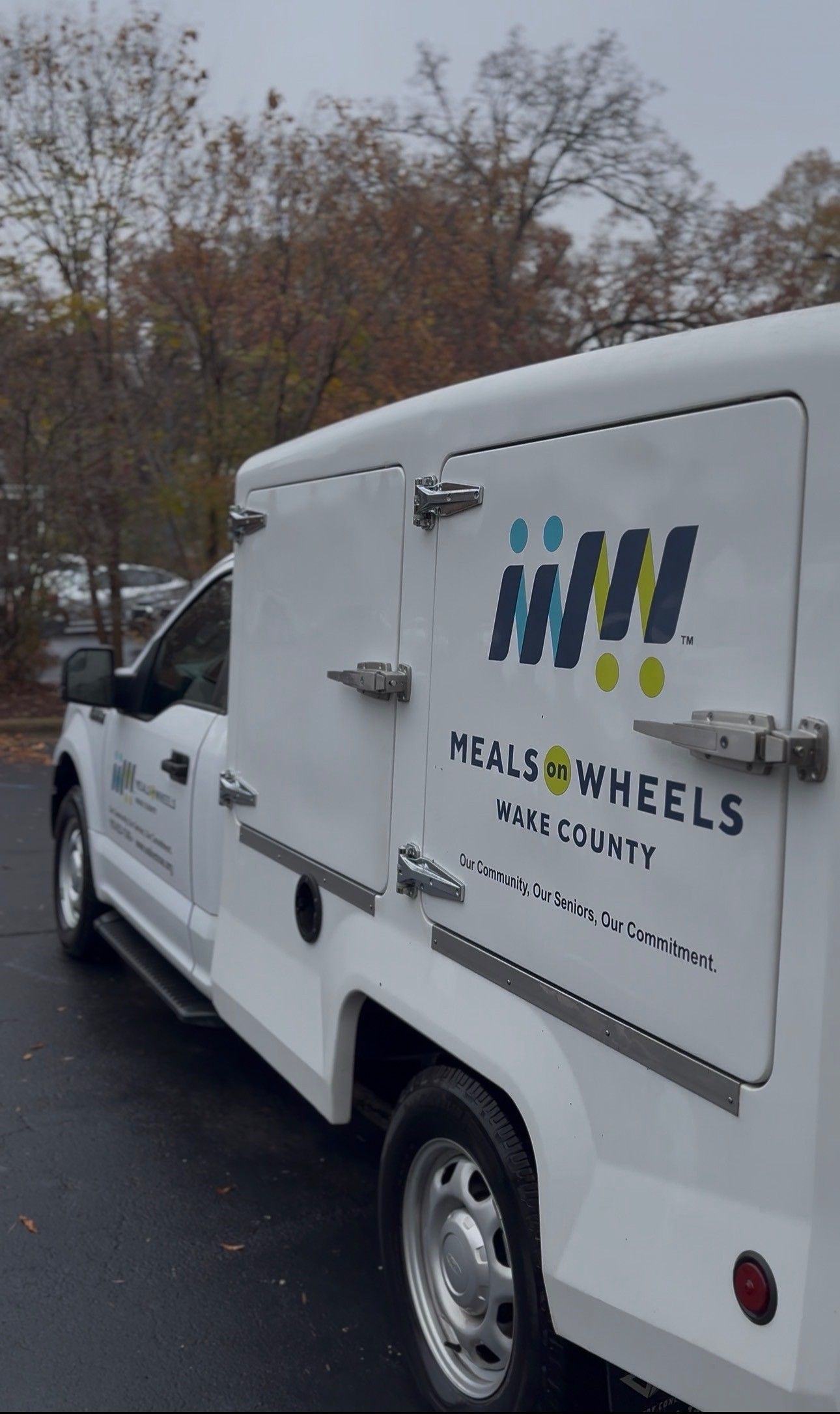 White Meals on Wheels truck with logo on the side, parked outside.