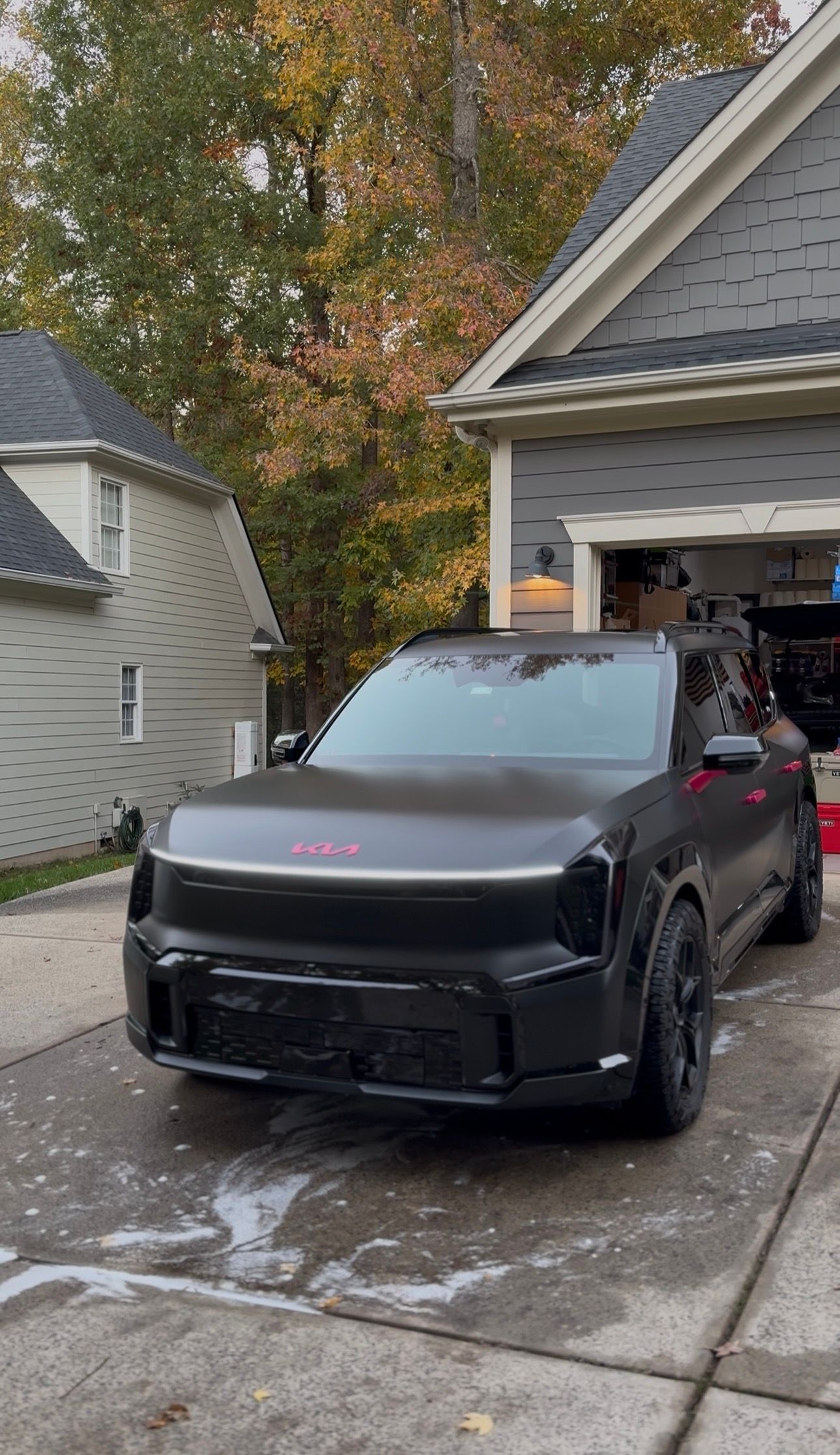 Black SUV being washed in a driveway with suds. House and trees in background.