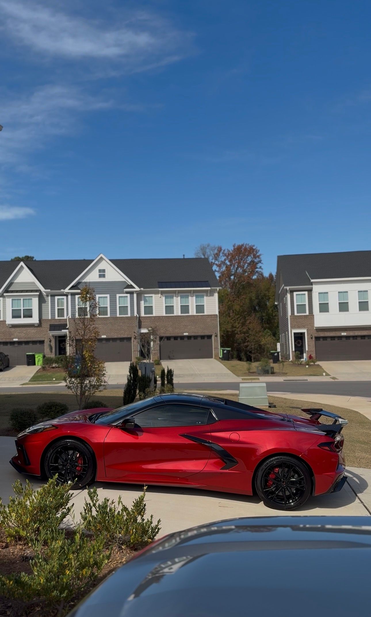 Red sports car parked on driveway, with townhouses and blue sky in the background.