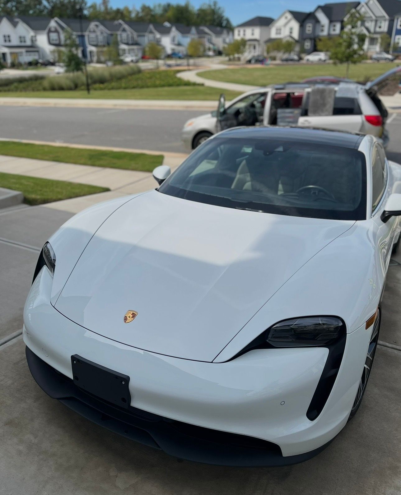 White Porsche Taycan parked on a driveway in front of a suburban neighborhood.