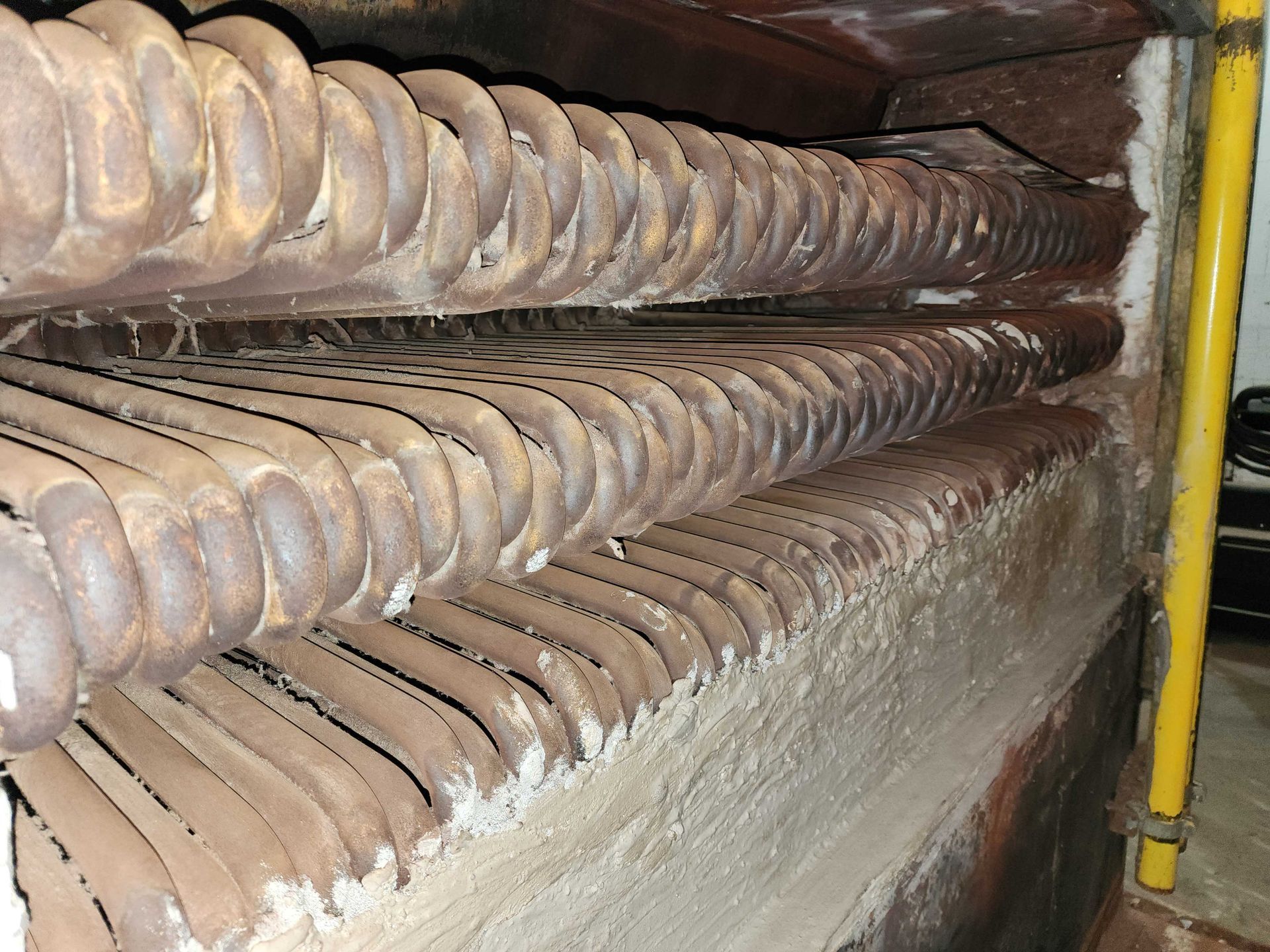 Rows of rusted, spiral metal tubes set in a brick-lined furnace.
