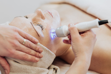 A woman is getting a clay mask on her face.