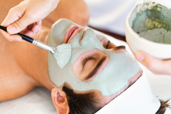 A woman is getting a clay mask on her face.