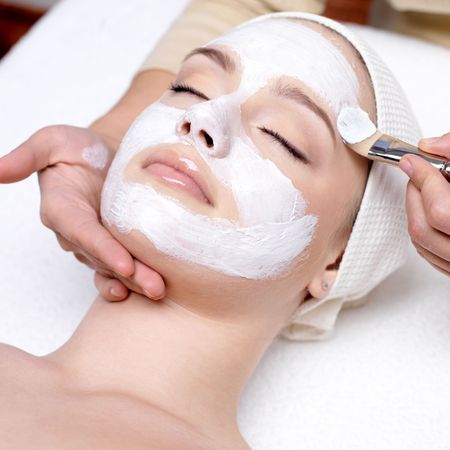 A woman is getting a white mask on her face.