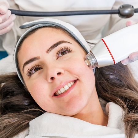 A woman is smiling while getting a treatment on her face