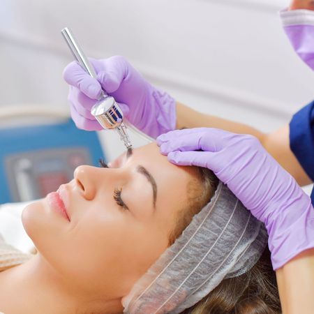 A woman wearing purple gloves is getting a facial treatment