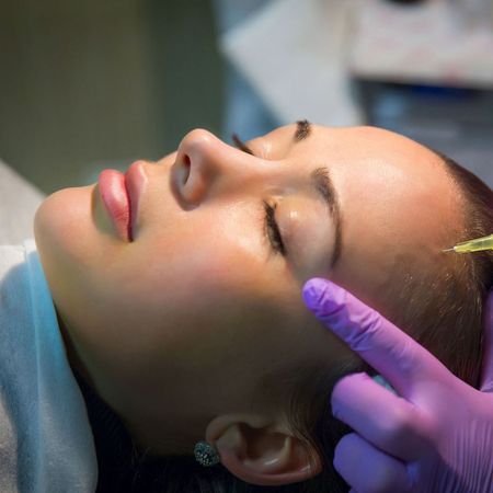 A woman is getting a facial treatment with purple gloves on