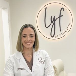 A woman in a lab coat is sitting in front of a sign for lyf aesthetics.