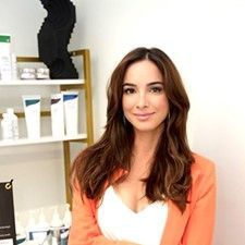 A woman in a lab coat is sitting in front of a sign for lyf aesthetics.