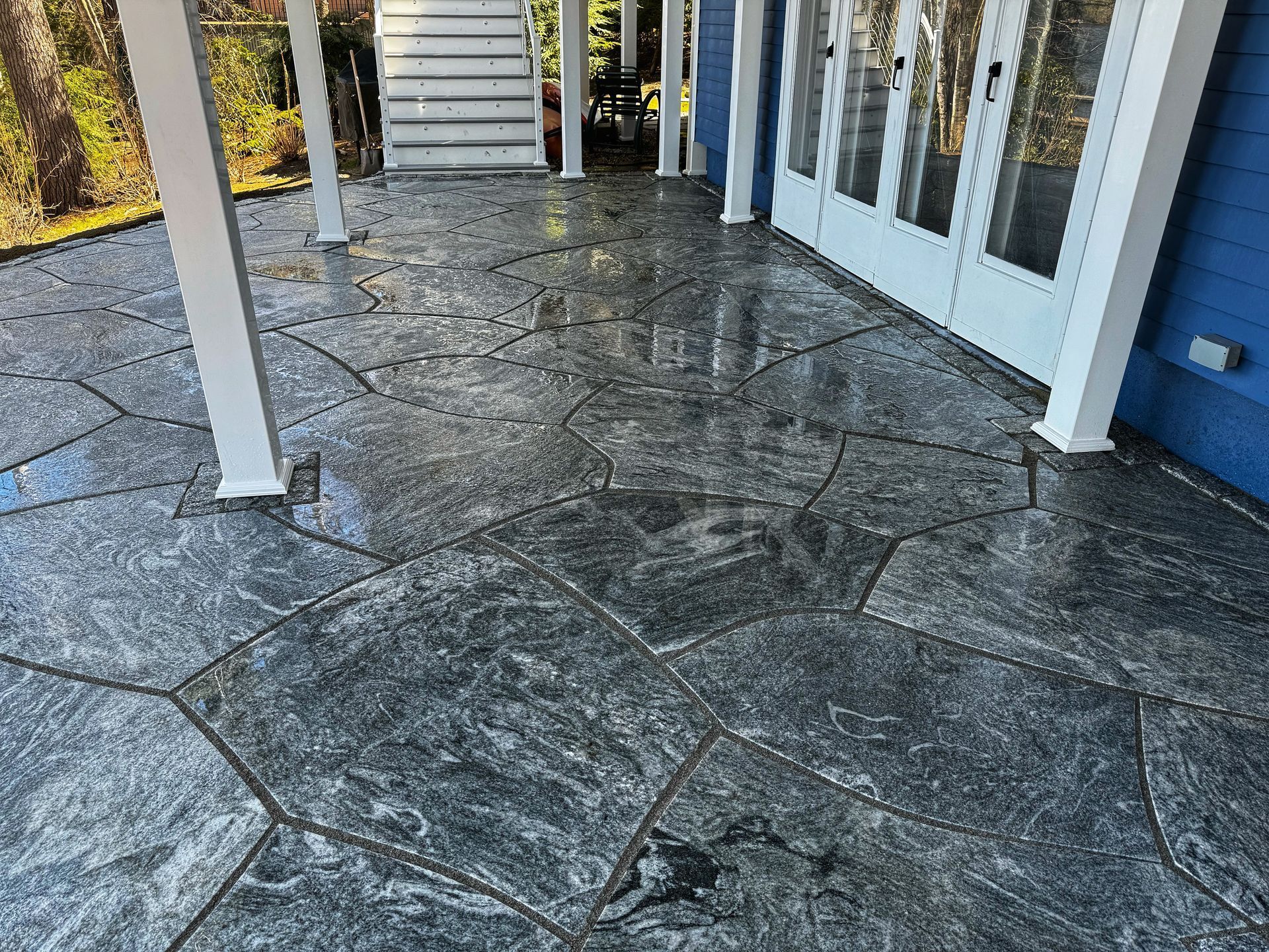 A grey flagstone-patterned patio surface under a wooden deck with white support posts.