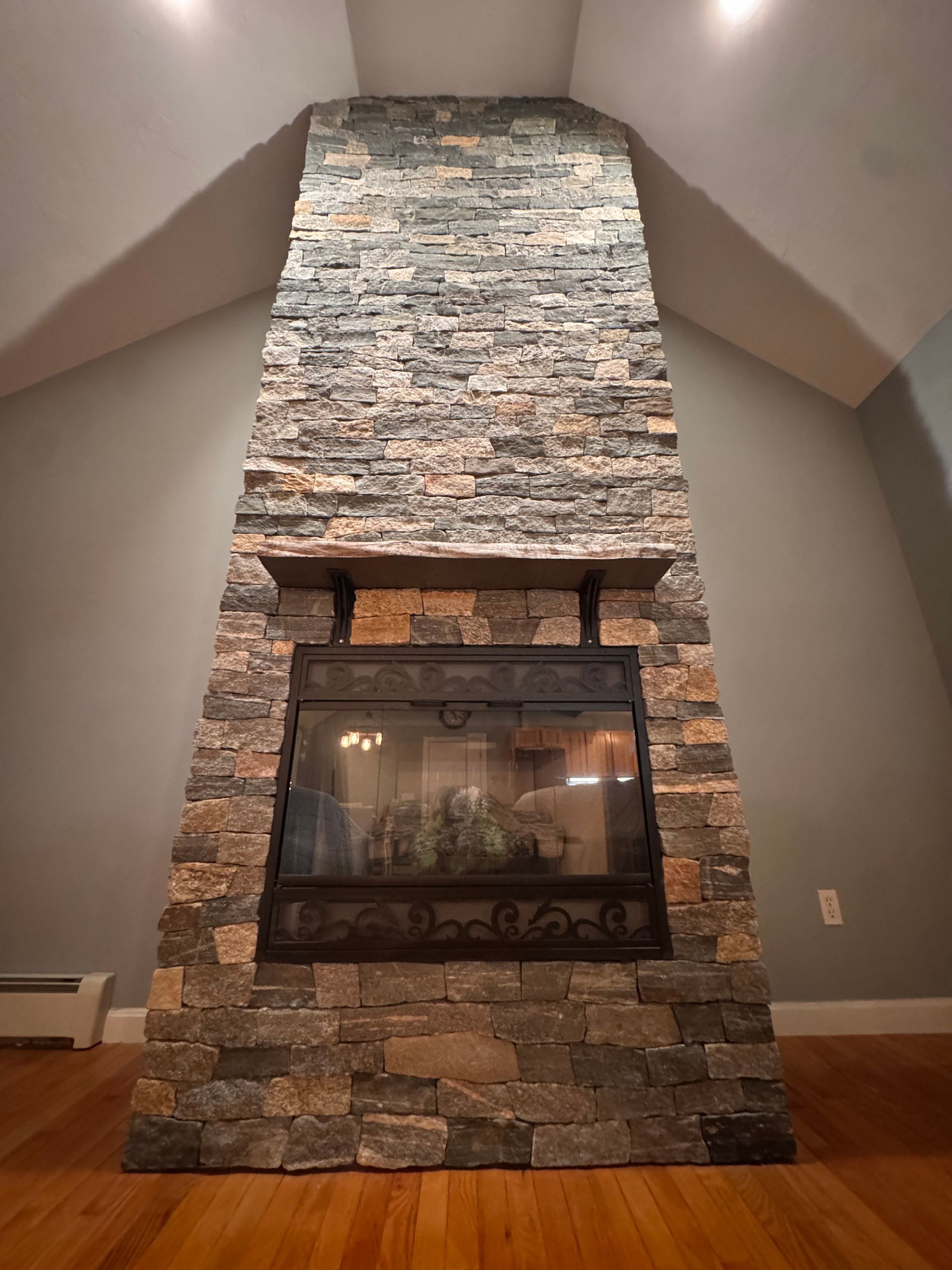 A floor-to-ceiling stone fireplace with a glass-front insert and a wooden mantel, set against light grey walls.