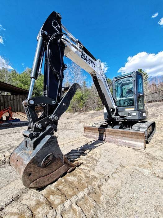 A white and black excavator parked on a dirt lot under a bright blue sky.