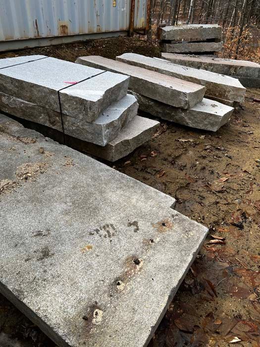 Stacked, rectangular granite slabs resting on a muddy, outdoor ground near a storage container.