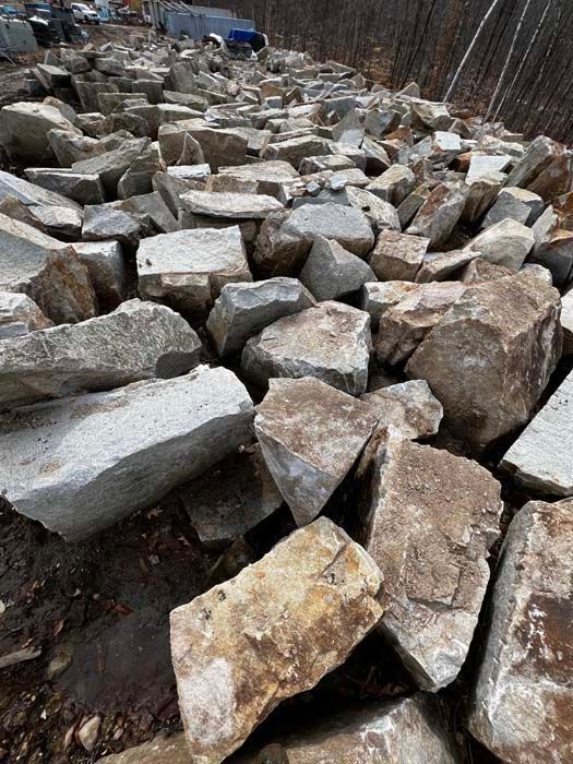 A large pile of angular, grey and tan rocks scattered on a dirt ground outdoors.